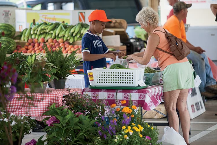 Young vendor helping a customer with fresh produce and flowers